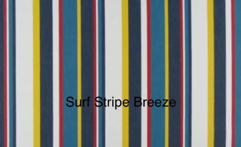 May include: A fabric pattern featuring vertical stripes in navy blue, white, yellow, red, and teal. The text Surf Stripe Breeze is printed in black across the center of the fabric, which displays a repeating sequence of these colored stripes.