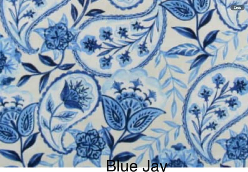May include: A fabric pattern featuring a white background with intricate blue paisley motifs, floral elements, and leafy vines. The design includes various shades of blue, ranging from light sky blue to deep navy, with the text Blue Jay at the bottom.
