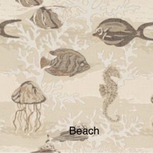 May include: A beige fabric featuring a repeating pattern of brown fish, jellyfish, and seahorses interspersed with white coral motifs. The word Beach is printed in black text near the bottom center of the design on the light background.