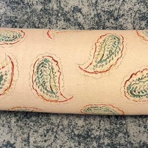 May include: A cylindrical bolster pillow featuring a light beige fabric base with a repeating paisley pattern in muted green and red tones. The ends of the bolster are finished with a solid light green piping trim along the circular edges.