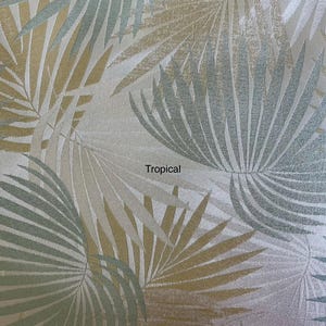 May include: A fabric featuring a repeating pattern of palm leaves in shades of metallic gold, soft blue, and white. The design includes the word Tropical printed in black text near the center, with a textured surface throughout the material.