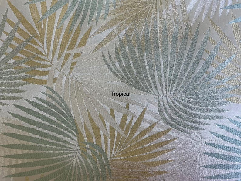 May include: A fabric featuring a repeating pattern of palm leaves in shades of metallic gold, soft blue, and white. The design includes the word Tropical printed in black text near the center, with a textured surface throughout the material.