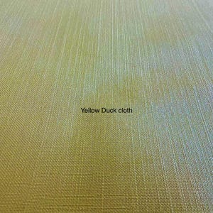 May include: A close-up view of yellow duck cloth fabric featuring a distinct, tightly woven texture with visible vertical and horizontal threads. The surface displays a uniform, matte yellow color throughout, with the text Yellow Duck cloth.