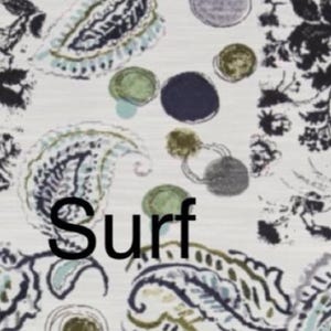 May include: A fabric pattern featuring a white background with black floral motifs, blue and green paisley shapes, and scattered dark blue and olive green circles. The word Surf is printed in black, bold, sans-serif capital letters across the center.