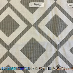 May include: A woven fabric featuring a repeating geometric pattern of large gray diamonds outlined by thick gray borders against a cream-colored background. The textile has a visible textured weave throughout, creating a consistent grid design.