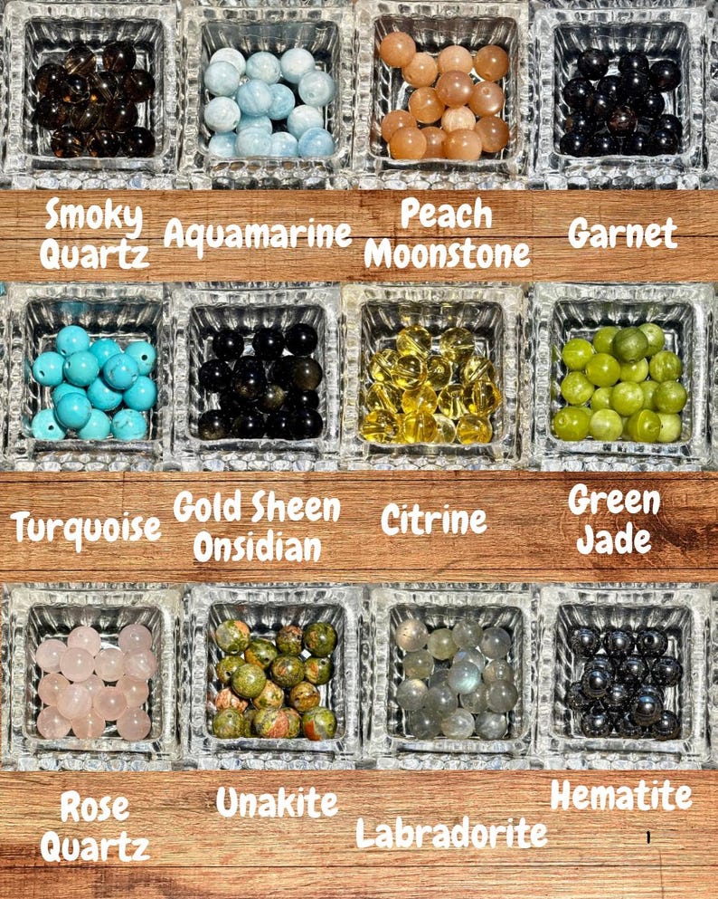 Op de afbeelding: Een verzameling edelsteen kralen in vierkante glazen bakjes. De kralen zijn in verschillende kleuren, waaronder rookkwarts, aquamarijn, perzikmaansteen, granaat, turkoois, goudglans obsidiaan, citrien, groene jade, rozenkwarts, unakiet, labradoriet en hematiet.