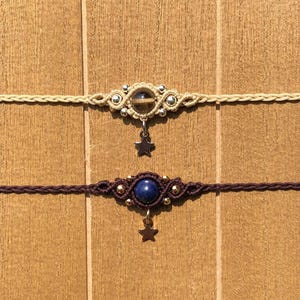 May include: Two macrame chokers with star pendants. One choker is beige with a clear stone and silver accents. The other is dark purple with a blue stone and gold accents. Both have a star charm hanging from the center.