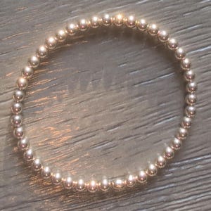 May include: A silver beaded bracelet. The bracelet is made of small, round, shiny silver beads strung together to form a circular shape. The beads reflect light, creating a bright and elegant appearance. The bracelet is a simple yet stylish piece of jewelry.