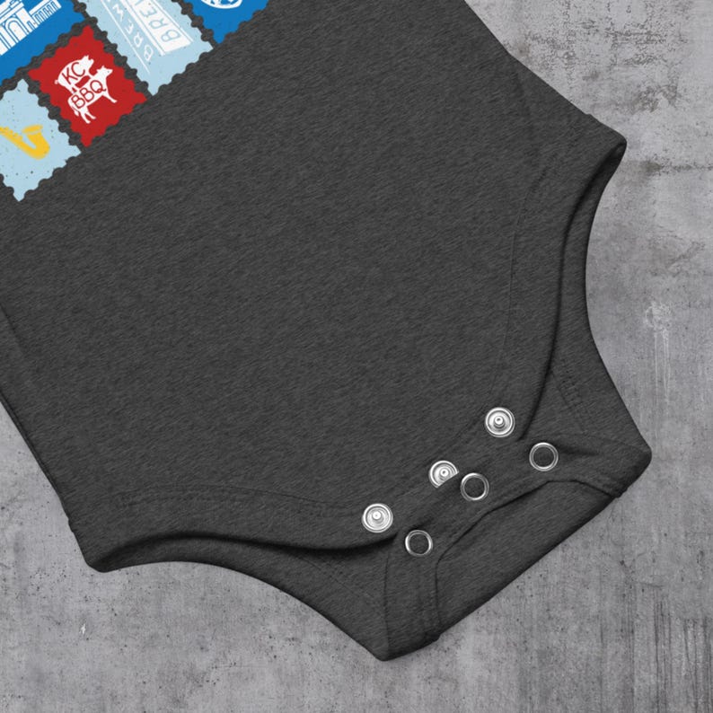 May include: Dark gray baby bodysuit with snap closures. The upper left corner features colorful postage stamp designs, including a red stamp with a pig and the text "KC BBQ".