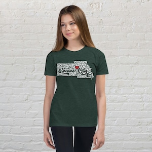 May include: Dark green t-shirt featuring a white outline of the state of Kansas with the words "Kansas City" in a decorative font. A red heart is placed over the city. The shirt is made of a soft material.