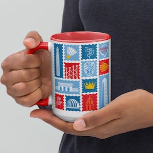May include: White ceramic mug with a red interior and handle, featuring a collage of blue, red, and yellow postage stamp-style designs. The stamps depict various Kansas City landmarks and the words "Kansas City" and "Brewery".