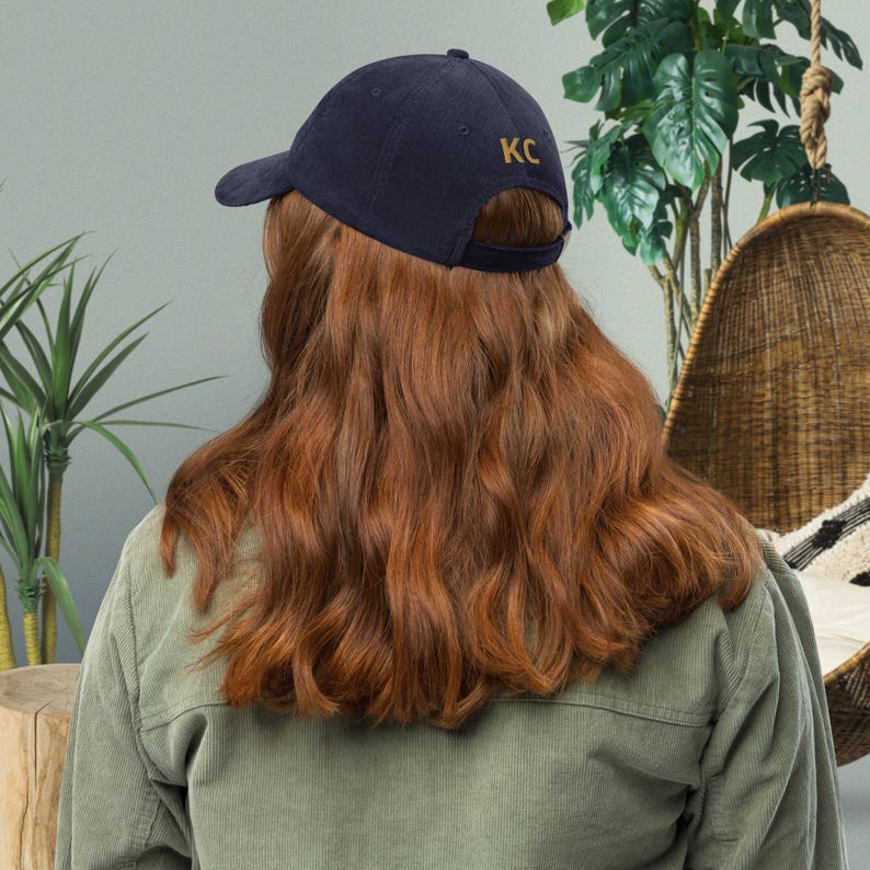 Puede incluir: Gorra de b&eacute;isbol azul marino con las letras doradas "KC" bordadas en la parte trasera. La gorra tiene una visera curva y una correa ajustable. Est&aacute; hecha de una tela suave y texturizada.
