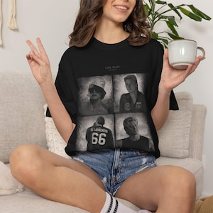 May include: A black short-sleeve t-shirt featuring a graphic print with the text THE PLOT. The design consists of four black and white photographic panels showing different individuals, including one wearing a jersey with DI LAURENTIS 66.