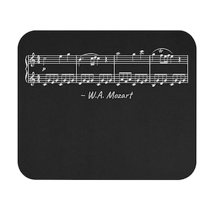 Op de afbeelding: Zwart rechthoekig muismat met witte muzieknoten en de tekst "~ W.A. Mozart". De muziekpartituur is gecentreerd op de mat. De mat heeft afgeronde hoeken.