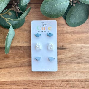 May include: A set of six stud earrings on a white card. The earrings are shaped like teapots, tea bags, and teacups in shades of blue and white. The card has the text "Too Cute clayworks" at the top and the shop's Etsy URL at the bottom.