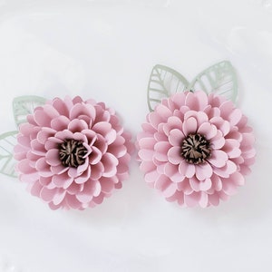 May include: Two pink paper flowers with green paper leaves. The flowers have a layered, ruffled appearance and a brown center.
