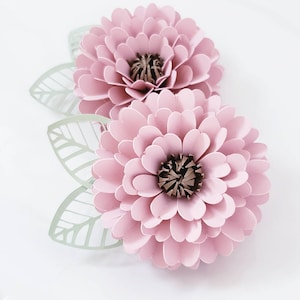 May include: Two pink paper flowers with green paper leaves. The flowers have a layered, 3D appearance.