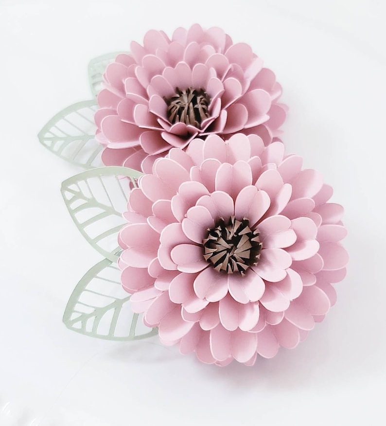 May include: Two pink paper flowers with green paper leaves. The flowers have a layered, 3D appearance.