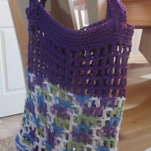 May include: A purple and multi-colored crocheted tote bag with a mesh design. The bag is hanging on a wooden chair.