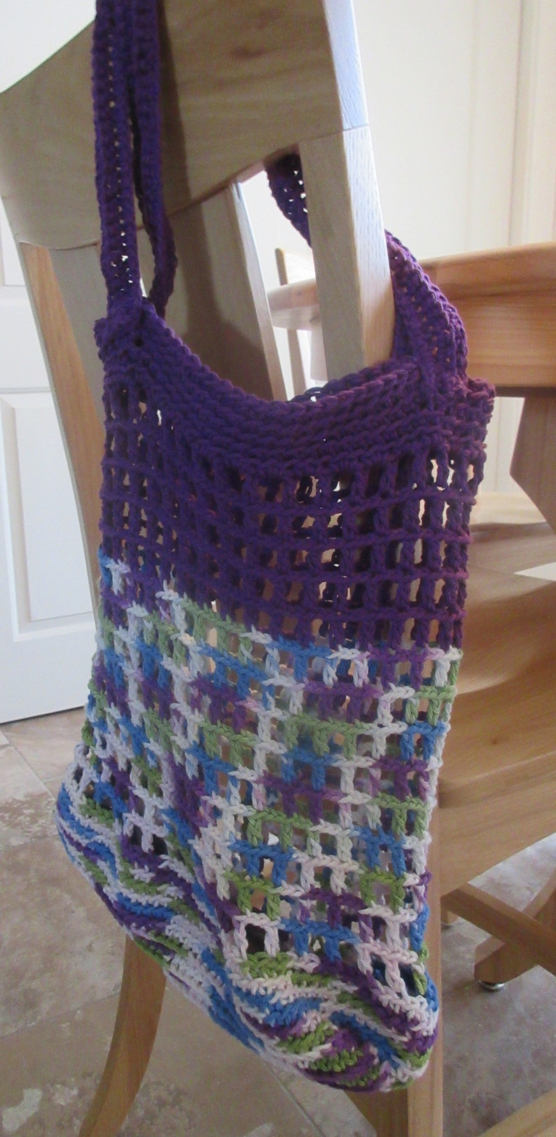 May include: A purple and multi-colored crocheted tote bag with a mesh design. The bag is hanging on a wooden chair.