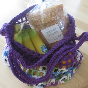 May include: Purple crochet string bag with a loaf of sesame seed Italian bread, bananas, and an orange. The bread has a "Freshness Guaranteed" sticker with a price of $1.99.