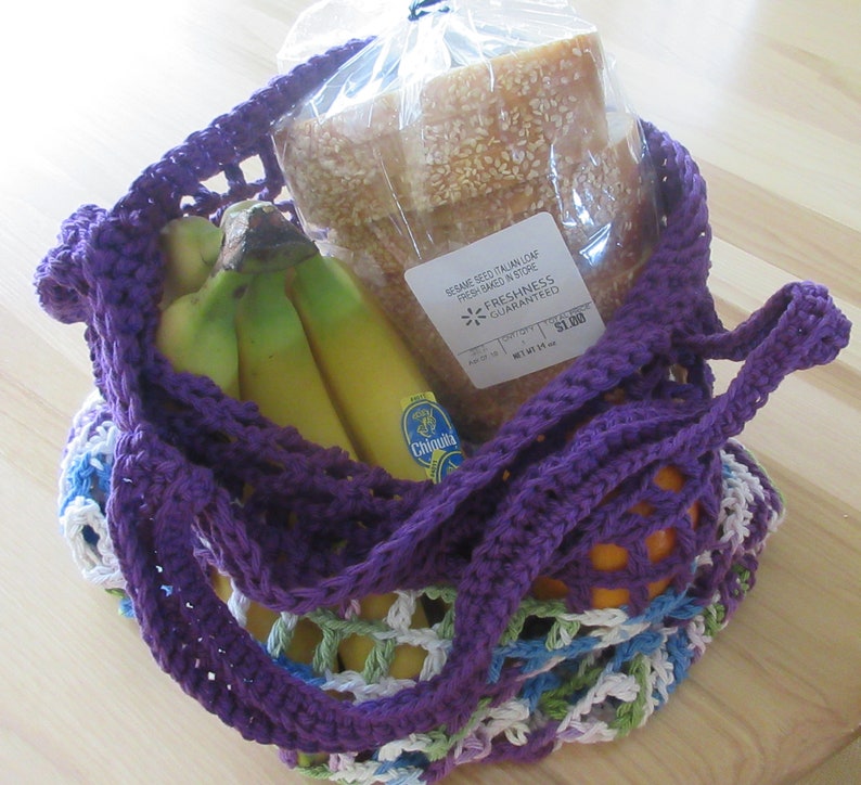 May include: Purple crochet string bag with a loaf of sesame seed Italian bread, bananas, and an orange. The bread has a "Freshness Guaranteed" sticker with a price of $1.99.