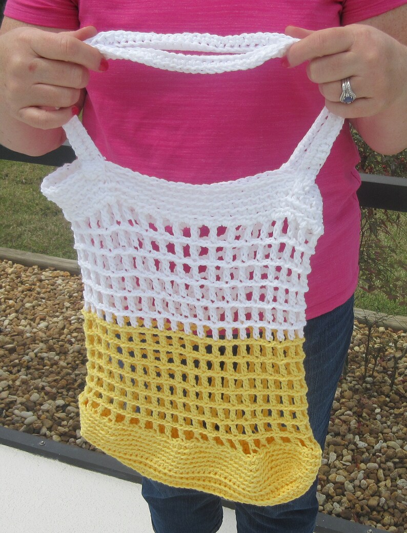 May include: A handmade crochet tote bag in white and yellow. The bag features a net-like design with a solid yellow bottom and white top. The bag has two white straps and a white handle.