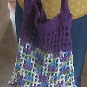 May include: A purple crocheted tote bag with a white, green, and blue patterned design. The bag has a wide, open top and two long straps.