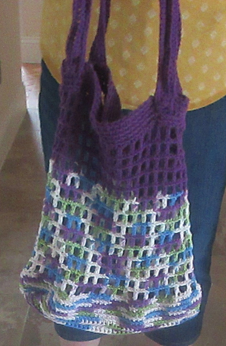 May include: A purple crocheted tote bag with a white, green, and blue patterned design. The bag has a wide, open top and two long straps.