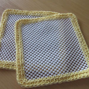 May include: Two yellow crocheted pot holders with a white mesh center. The pot holders are square shaped and have a crocheted border.