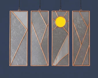 May include: Four rectangular stained glass panels hanging from thin black chains. Each panel features clear textured glass segments framed in copper, with one panel displaying a bright yellow circular sun design at the top.