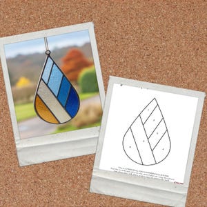 Pode incluir: Um apanhador de sol em forma de l&aacute;grima de vitral com uma moldura de metal preta. O design apresenta sec&ccedil;&otilde;es douradas, prateadas e tons de azul. Um padr&atilde;o para o apanhador de sol tamb&eacute;m &eacute; mostrado.