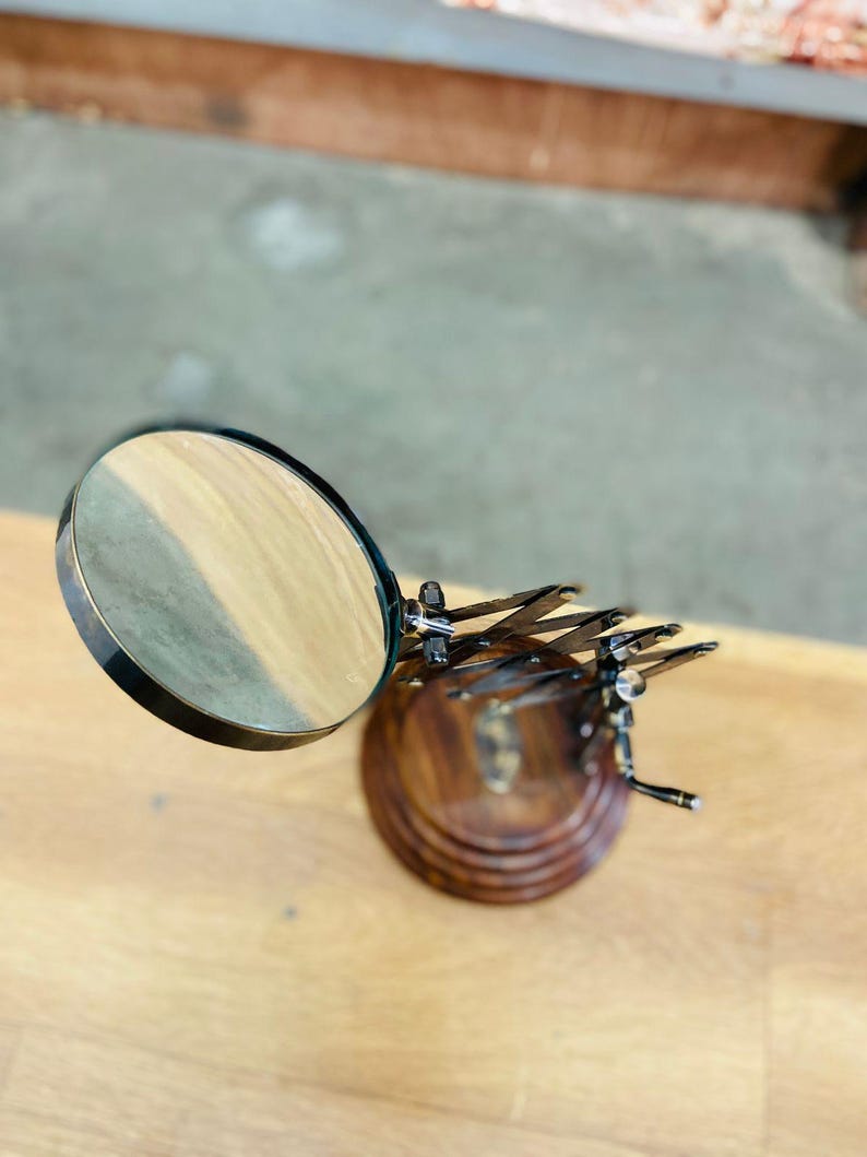 May include: A magnifying glass with a round lens and a dark metal frame. The lens is positioned above a wooden base with a decorative metal dragonfly design. The base is made of dark wood.