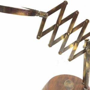 May include: A vintage-style brass magnifying glass with an adjustable scissor arm and a wooden base. The magnifying glass features a rectangular lens and a handle. The brass components have a warm, aged patina, adding to its antique aesthetic.