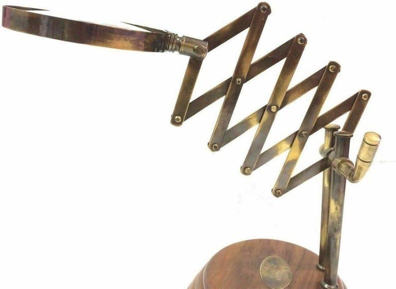 May include: A vintage-style brass magnifying glass with an adjustable scissor arm and a wooden base. The magnifying glass features a rectangular lens and a handle. The brass components have a warm, aged patina, adding to its antique aesthetic.