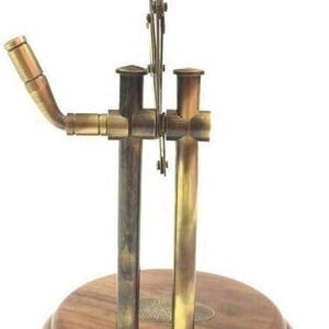 May include: A vintage-style magnifying glass with a brass frame and a wooden base. The magnifying glass is mounted on a brass mechanism with a curved arm. The base is a dark, tiered wood. The overall design is reminiscent of antique scientific instruments.
