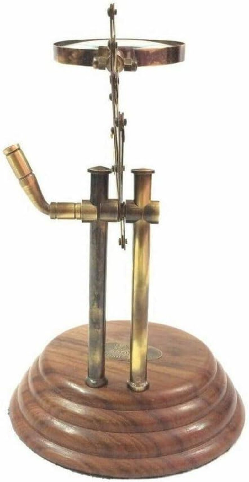 May include: A vintage-style magnifying glass with a brass frame and a wooden base. The magnifying glass is mounted on a brass mechanism with a curved arm. The base is a dark, tiered wood. The overall design is reminiscent of antique scientific instruments.
