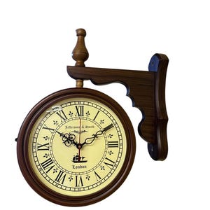 May include: A double-sided wall clock with a dark brown wooden frame and a cream-colored face. The clock features Roman numerals, black hands, and the text "Jefferson & Smith London". The clock is mounted on a decorative wooden bracket.