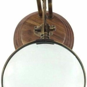 May include: A vintage-style magnifying glass with a round lens and a brass frame. The magnifying glass is mounted on a wooden base with brass hardware. The design is reminiscent of antique scientific instruments.