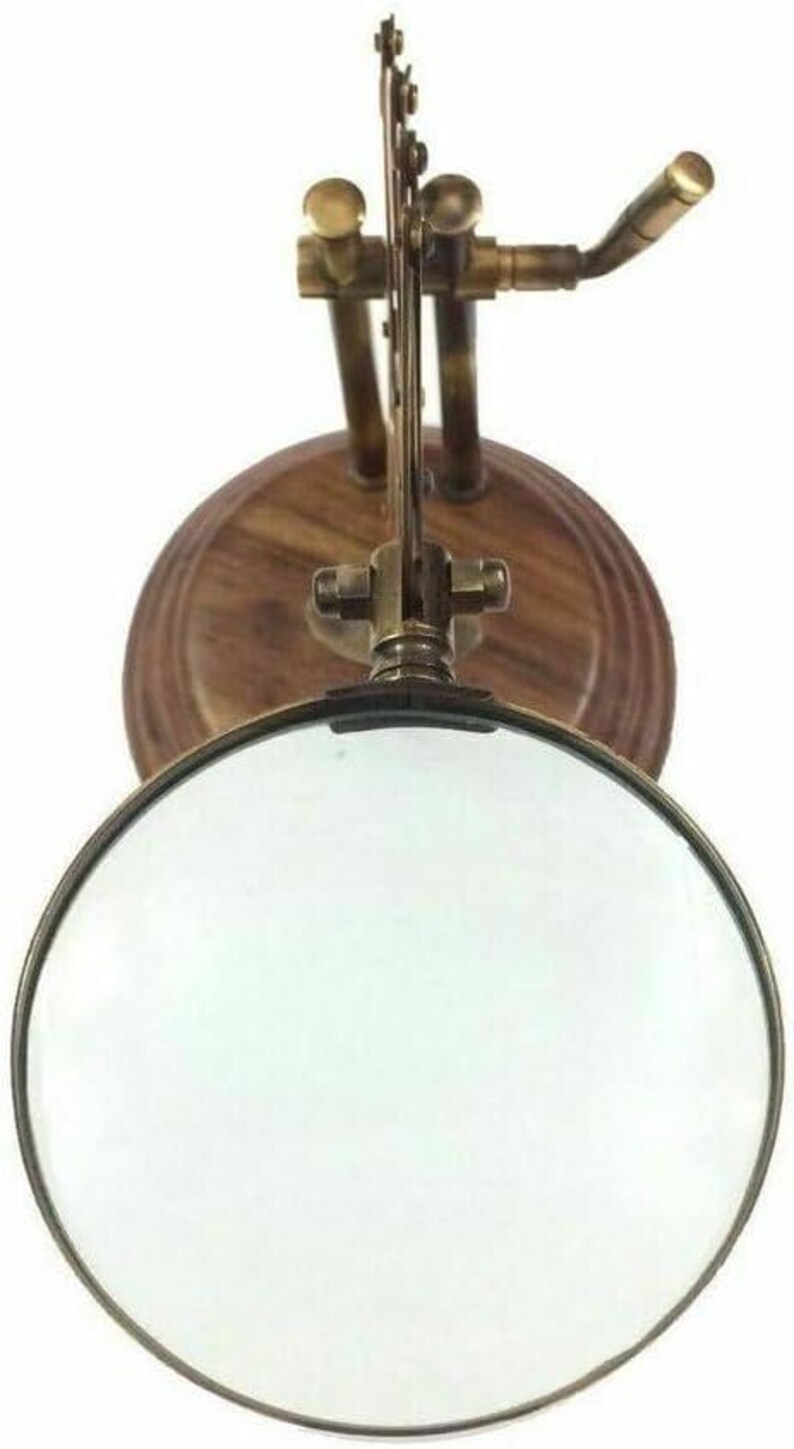 May include: A vintage-style magnifying glass with a round lens and a brass frame. The magnifying glass is mounted on a wooden base with brass hardware. The design is reminiscent of antique scientific instruments.