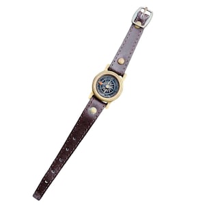 Op de afbeelding: Een vintage kompas horloge met een donkerbruine leren band en een messingkleurig kompas gezicht. Het kompas heeft een gedetailleerde wijzerplaat en een kleine gesp. Het horloge is ontworpen voor outdoor liefhebbers.