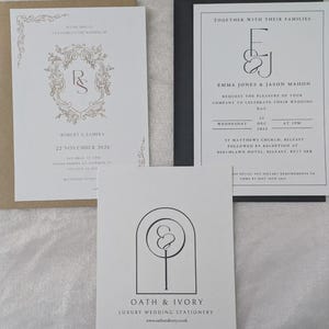 May include: Three wedding stationery cards. One white card with gold ornate frame and text Robert & Samira 22 November 2026 in a tan envelope. One white card with black text E&J Emma Jones & Jason Mahon in a black envelope. One white card with Oath & Ivory logo.