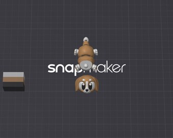 May include: A 3D model of a brown and white dog figure, shown in two separate parts: the head and the body. The text "snapmaker" is displayed in white letters behind the figure, and a small rectangular block with gray, brown, and black stripes is visible.