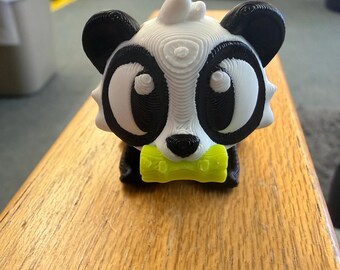 May include: A 3D printed panda figurine featuring a white and black head with large eyes, a small black nose, and a bright lime green bamboo stalk held in its mouth. The surface displays visible horizontal layer lines from the printing process.