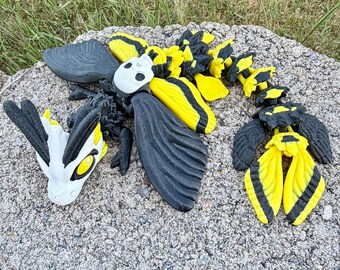 May include: An articulated dragon figure featuring a white head with yellow eyes and black accents, a black and yellow segmented body, and large black wings. The creature has a white skull-like piece on its back and a long, flexible tail.