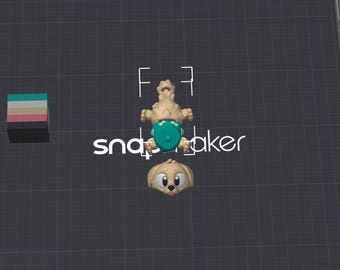 May include: A 3D model of a tan puppy figure with a separate head and body, featuring a teal diaper with white bone patterns. To the left is a small stack of colored blocks in teal, white, pink, and black. The text snapmaker is visible in white.