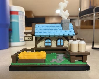 May include: A miniature 3D printed farm building with a blue roof, a chimney with white smoke, and a sign that reads MOO!. The scene includes a yellow hay bale, a brown fence, a stone path, and a wooden table holding four small milk bottles.