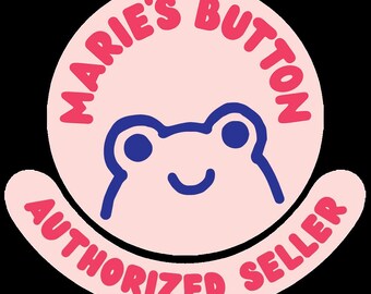 May include: A circular pink button featuring a dark blue line drawing of a frog face in the center. The text MARIE'S BUTTON is arched across the top in pink, and the text AUTHORIZED SELLER is arched along the bottom in pink.