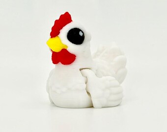 May include: A small white chicken figurine featuring a bright red comb and wattle, a yellow beak, and large black eyes. The figure has a textured surface with visible layered details, depicting a sitting bird with folded wings and a rounded body.