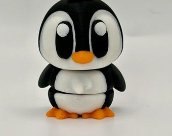 May include: A small 3D printed penguin figurine featuring a black and white body, large white eyes with black pupils, a bright orange beak, and orange feet. The surface shows visible horizontal layer lines from the additive manufacturing process.
